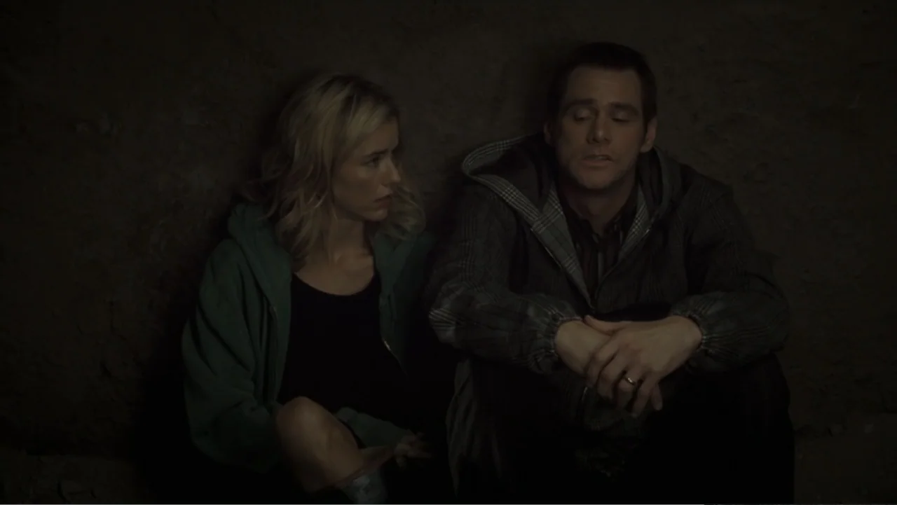 Fun with Dick and Jane (2005) movie still: medium — A dark, dimly lit space with rough stone-like walls. A man and woman sit side-by-side on the…