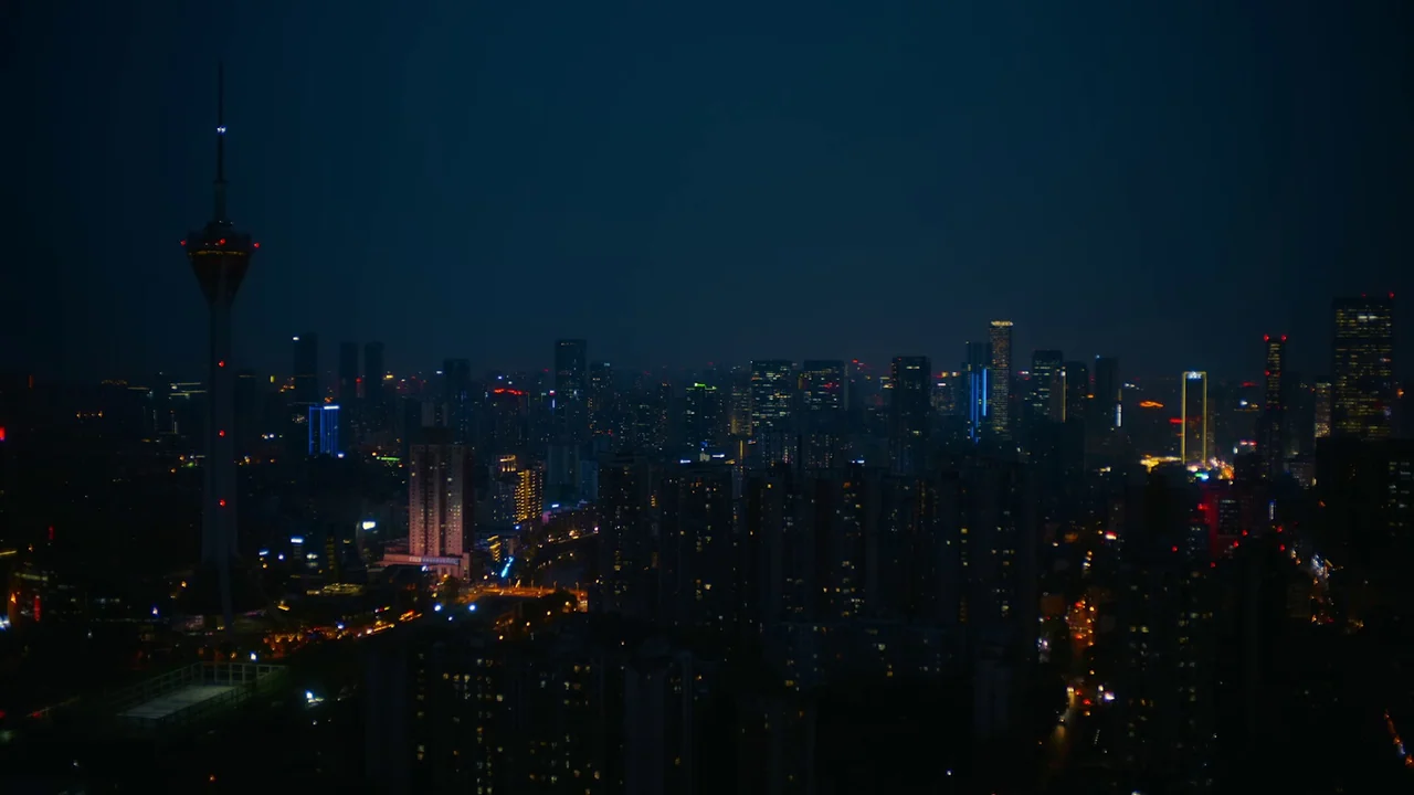 The Last Year of Darkness (2023) movie still: establishing — A dense urban skyline at night viewed from a high vantage point. A tall radio tower…