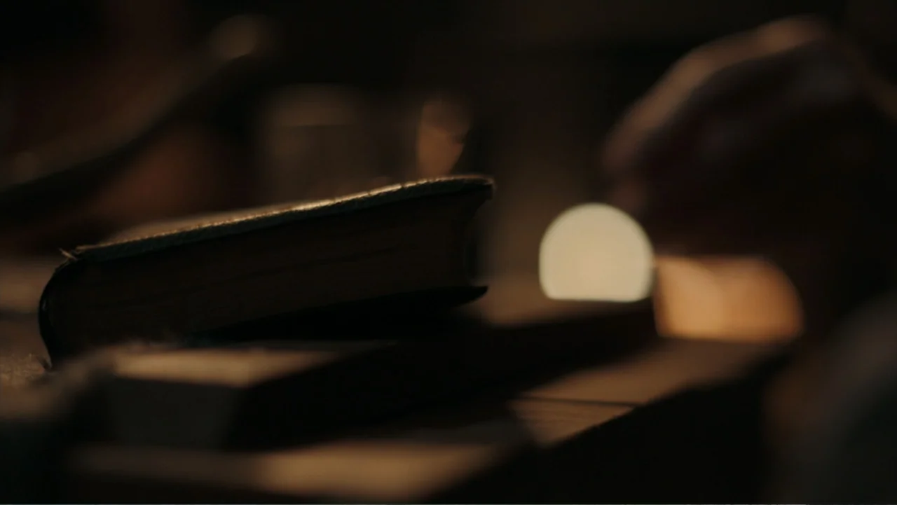 Alabama Snake (2020) movie still: closeup — A small, thick closed book sits on a dark, out-of-focus wooden surface. A soft, warm circular light glow…
