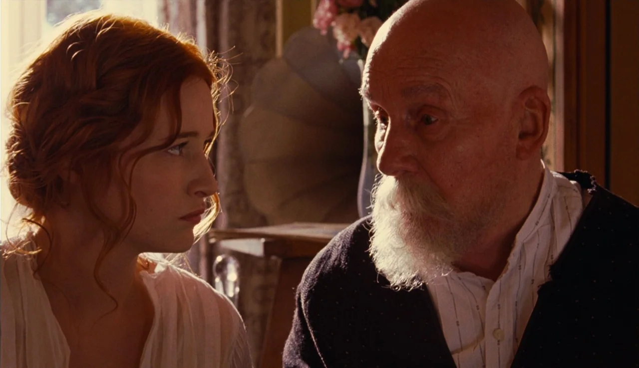 Renoir (2012) movie still: medium — An interior space contains a young woman and an elderly man facing one another. The man has a white beard and…