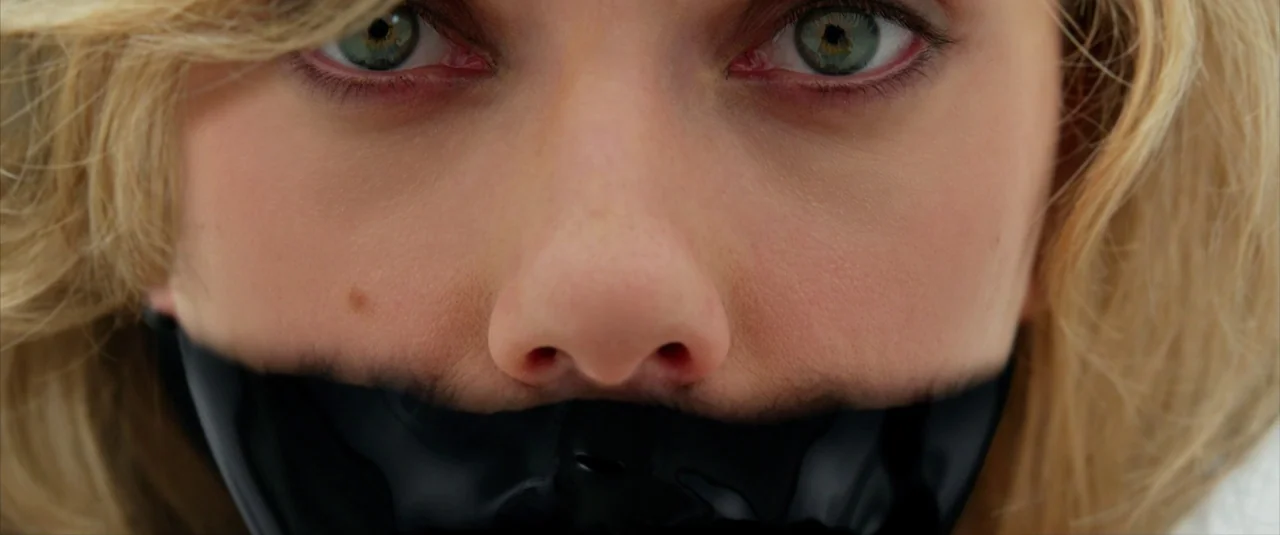 Lucy (2014) movie still: closeup — A close-up view of a woman's eyes and nose with her mouth taped shut. Black tape covers the lower face while…