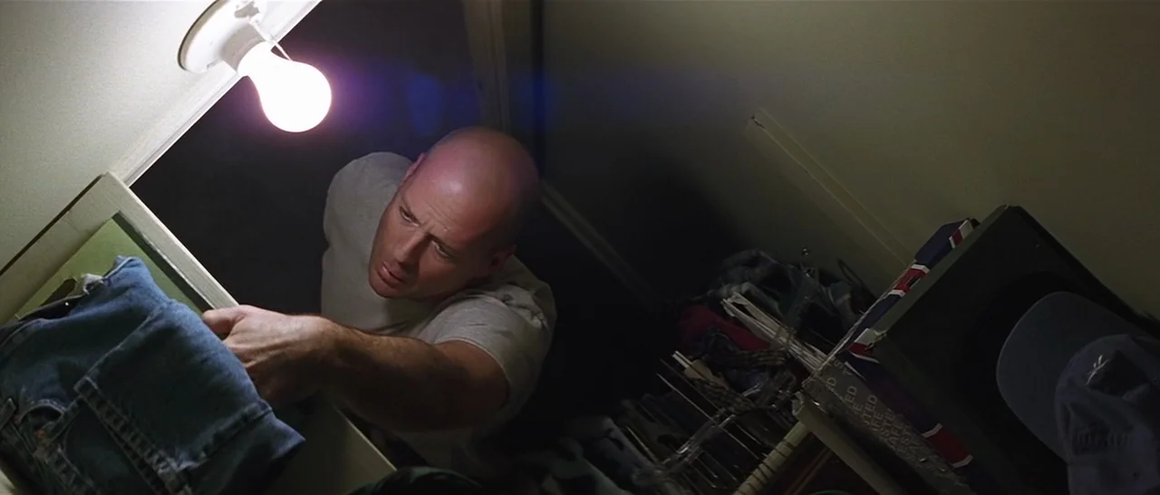 Unbreakable (2000) movie still: medium — A small cluttered closet contains shelves stacked with folded clothes and miscellaneous household items. A…