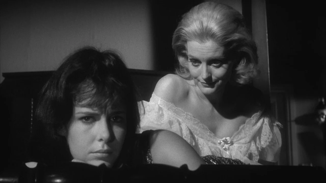 The Naked Kiss (1964) movie still: medium — A dimly lit bedroom with shadows obscuring most of the surrounding architectural details. Two women are…