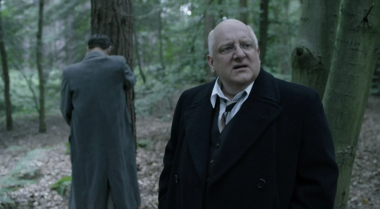 The Death of Stalin (2017) movie still: medium — A dense wooded area with tall trees and scattered fallen leaves on the ground. An older man in a…
