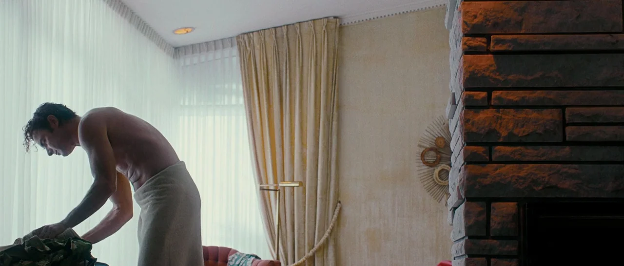 Pawn Sacrifice (2014) movie still: medium — A 1970s hotel interior features floor-to-ceiling sheer curtains and a stone fireplace pillar. A…
