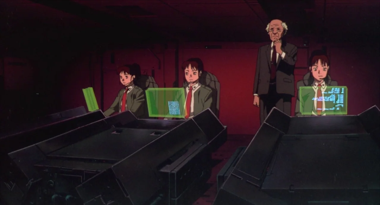 Ghost in the Shell (1995) movie still: wide — A dimly lit room bathed in red light features multiple technological workstations for operators. Three…