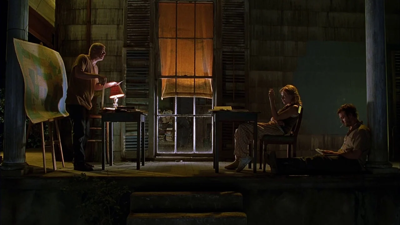 Love Song For Bobby Long (2004) movie still: wide — A wooden porch at night contains a map on an easel and two tables. Three people occupy the space…