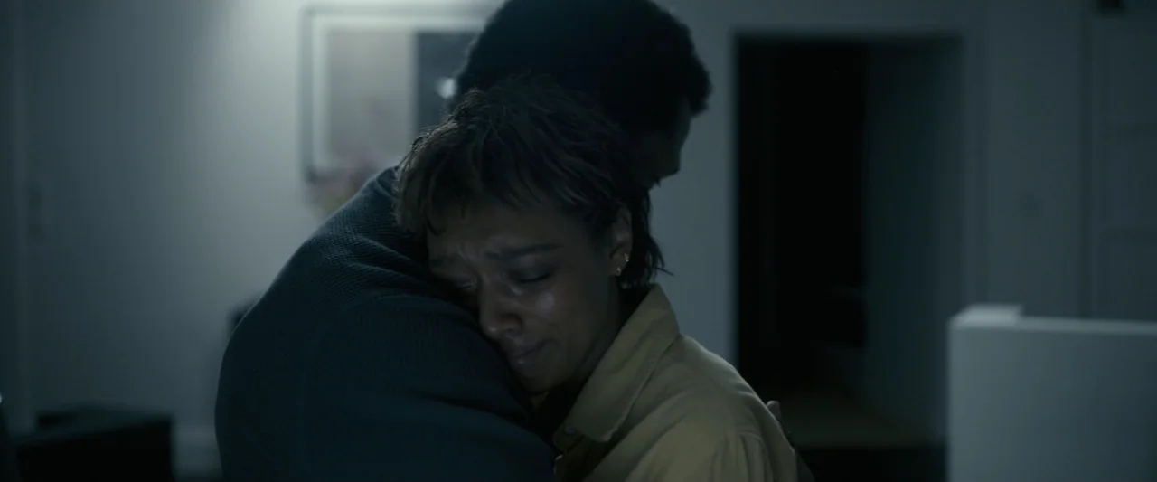 Talk to Me (2023) movie still: closeup — A dimly lit room serves as the backdrop for two people embracing closely. A woman is crying while resting…