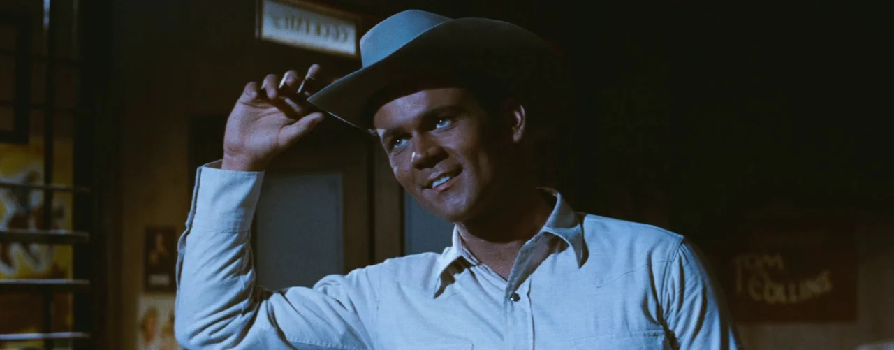Bus Stop (1956) movie still: medium — A dimly lit drinking establishment features a sign advertising Tom Collins in the background. A man wearing a…