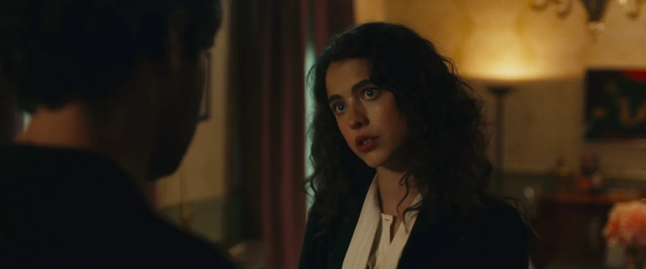 Sanctuary (2023) movie still: medium — A dimly lit room with muted wall colors and a warm standing floor lamp. A woman with dark curly hair looks…