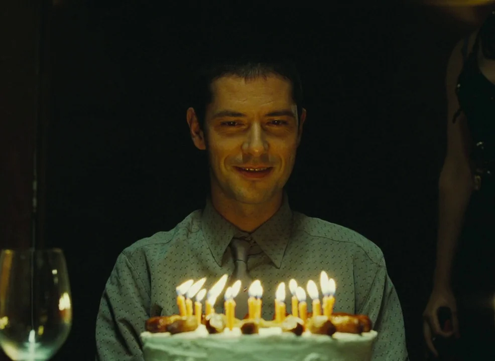 Laurence Anyways (2012) movie still: medium — A dark indoor space where a man sits holding a lit birthday cake. The candles provide the only…