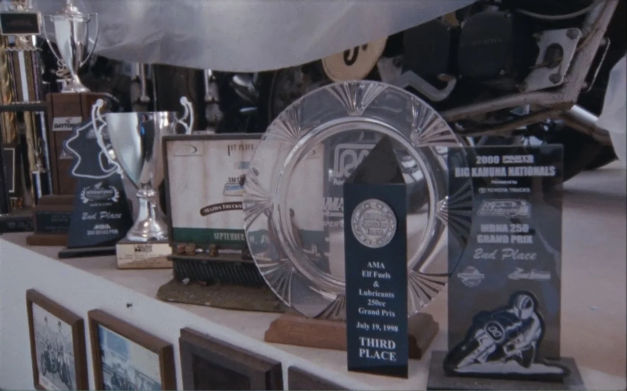 The Greasy Hands Preachers (2014) movie still: medium — A collection of silver cups and acrylic award plaques sits on a display shelf. The trophies…