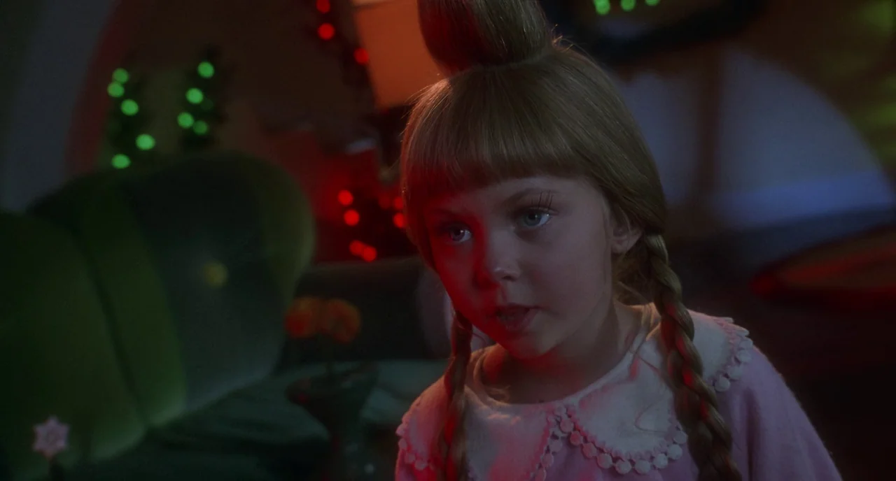 How The Grinch Stole Christmas (2000) movie still: closeup — A dimly lit room decorated with oversized colorful furniture and stylized festive…