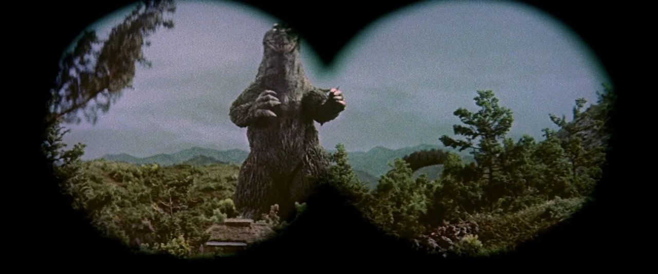 King Kong Vs. Godzilla (1962) movie still: wide — A mountainous landscape with dense greenery and a small hut in the foreground. A large bipedal…