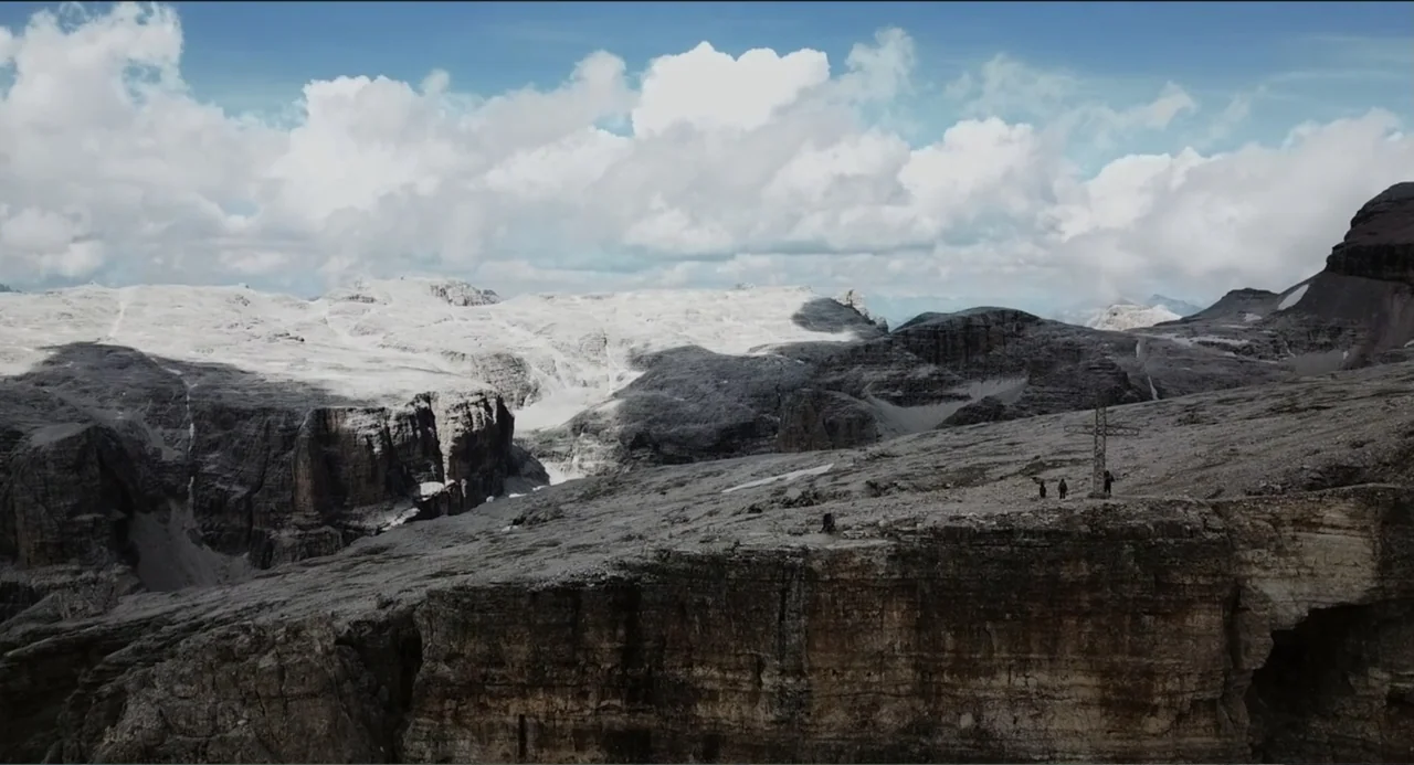 Crooked Trees Gon Give Me Wings (2022) movie still: establishing — A high-altitude mountain range features craggy grey rock faces and patches of…
