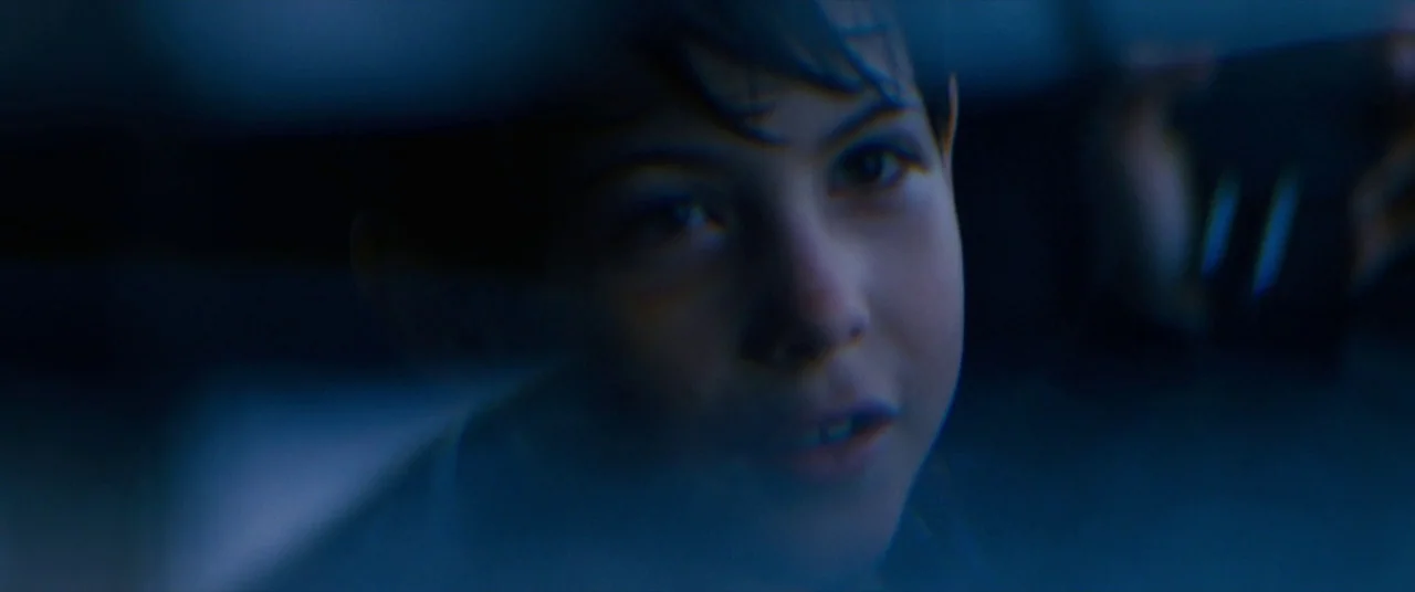 The Death and Life of John F. Donovan (2018) movie still: closeup — A dark, blurred interior space surrounds a child's face in low light. The…