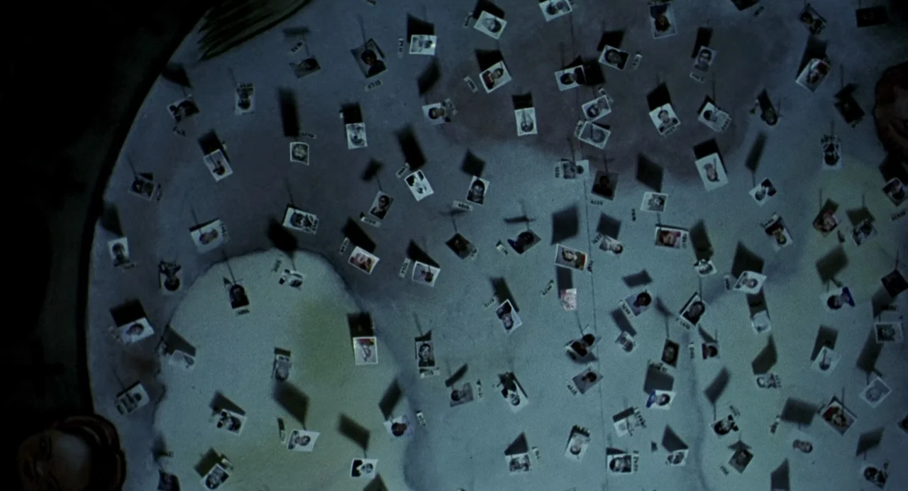 The Nameless (1999) movie still: wide — A dark, textured surface is covered in numerous small individual portraits arranged irregularly. Each…