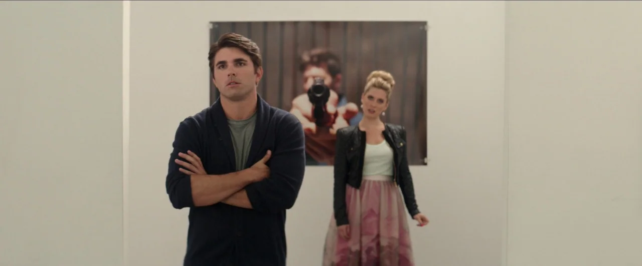 Dean (2016) movie still: medium — A man and woman stand in a white art gallery featuring a large photograph. The photograph depicts a person…