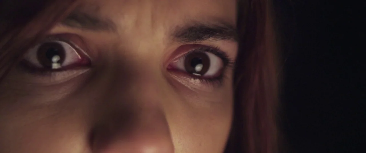 Here Comes The Devil (2012) movie still: closeup — A close-up of a person's eyes against a dark, featureless backdrop. The subject stares directly…