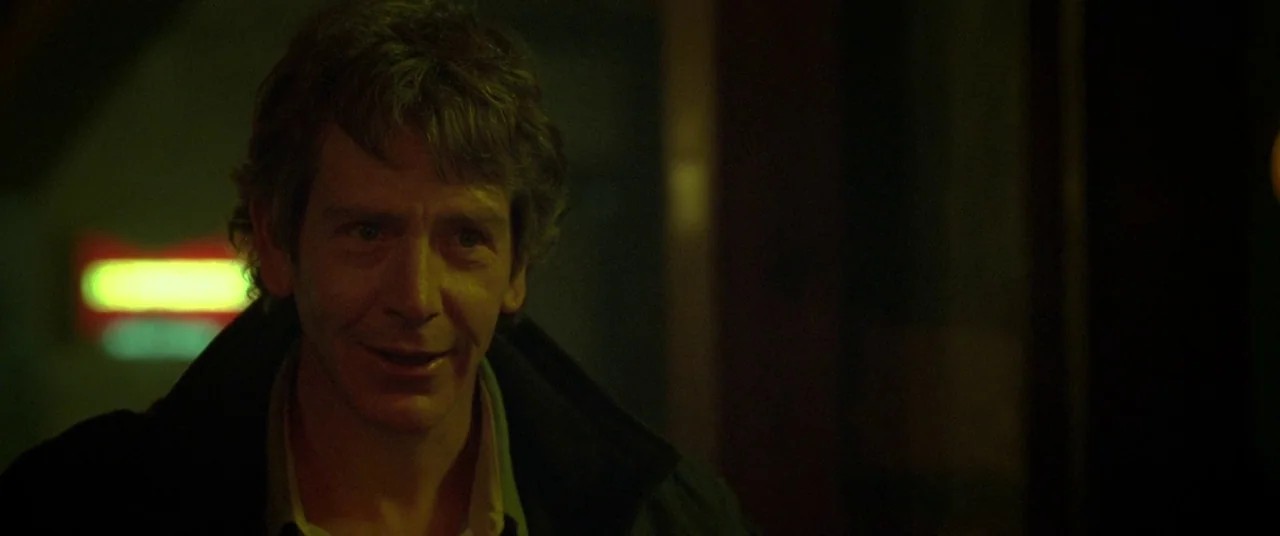 Mississippi Grind (2015) movie still: closeup — A dimly lit interior with a blurry neon sign visible in the dark background. A middle-aged man with…