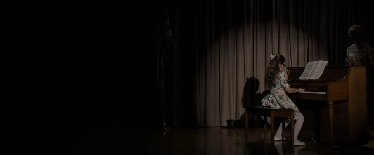 Equation of Love and Tone Deafness (2015) movie still: medium — A dark auditorium stage features a single spotlight on a girl playing the piano. An…