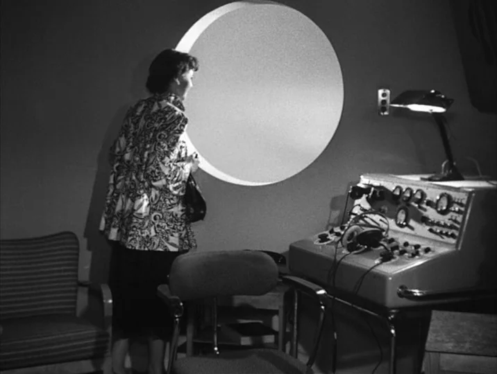 To Joy (1950) movie still: medium — A spartan room features a large circular window and a technical control station. A woman stands in profile…