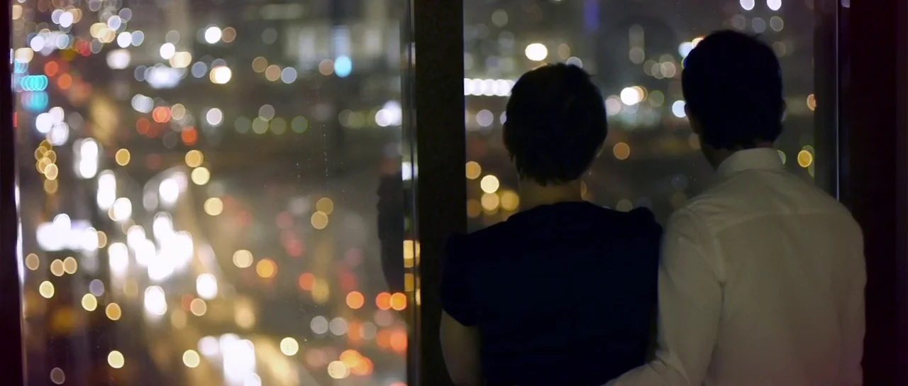 Upstream Color (2013) movie still: medium — A couple looks out of a window from a high-rise building at night. City traffic lights create bright,…