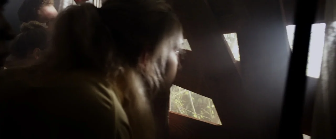 Mermaid Down (2019) movie still: closeup — A dimly lit interior space features walls constructed with vertical wooden planks and horizontal slits. A…