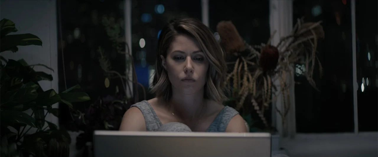 Equation of Love and Tone Deafness (2015) movie still: medium — A dimly lit indoor space at night with large windows showing distant city lights. A…