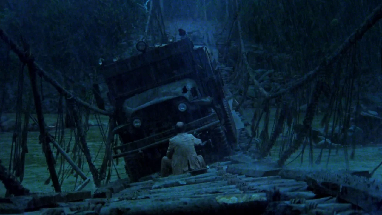 Sorcerer (1977) movie still: wide — A rain-slicked wooden suspension bridge crosses a river during a dark stormy night. A large military-style truck…