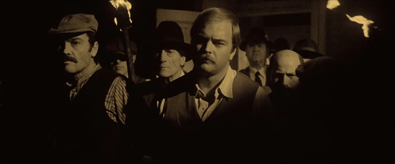 The Beyond (1981) movie still: medium — A group of men walks through a dark environment illuminated by hand-held torches. The figures move in a…