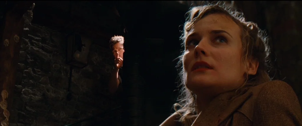 Inglourious Basterds (2009) movie still: medium — A dimly lit stone chamber with rough masonry walls and deep pockets of shadow. A woman in a tan…