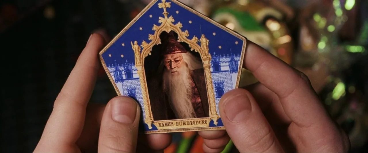 Harry Potter and the Philosopher's Stone (2001) movie still: closeup — Close-up of human hands holding a blue and gold magical trading card. The…