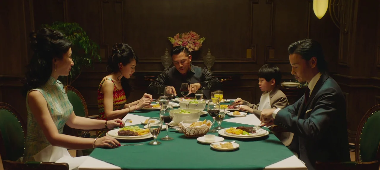 Master Z: The Ip Man Legacy (2018) movie still: wide — A dimly lit, wood-paneled dining room contains a formal table with a green cloth. Five people…