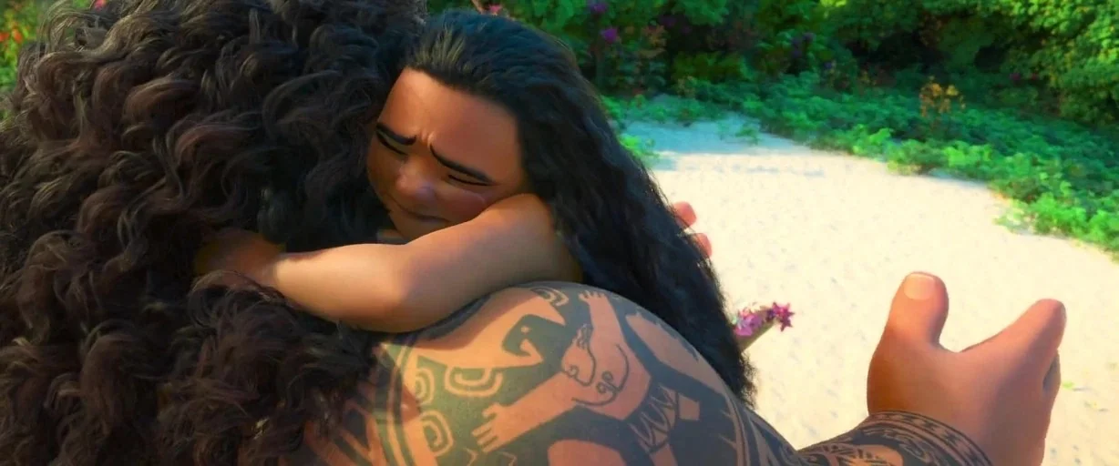 Moana (2016) movie still: closeup — A sunny tropical coastline features a sandy shore and dense green vegetation. A child holds onto the back of a…