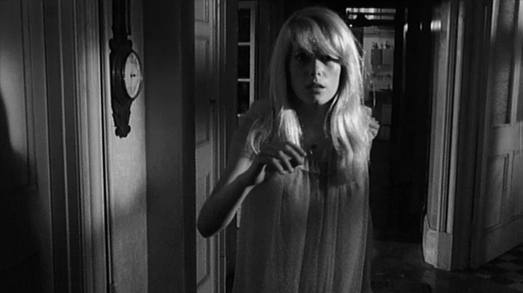 Repulsion (1965) movie still: medium — A dimly lit residential hallway at night features a wall-mounted analog clock. A blonde woman in a nightgown…