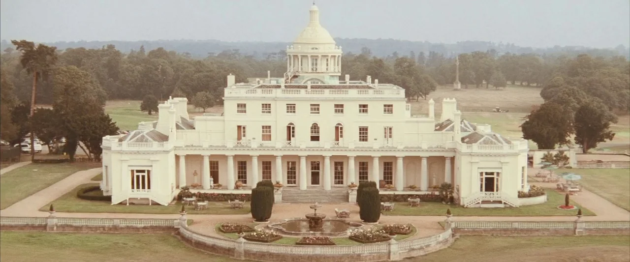 Layer Cake (2004) movie still: establishing — A large neoclassical estate with a central dome sits surrounded by manicured lawns. A tiered fountain…