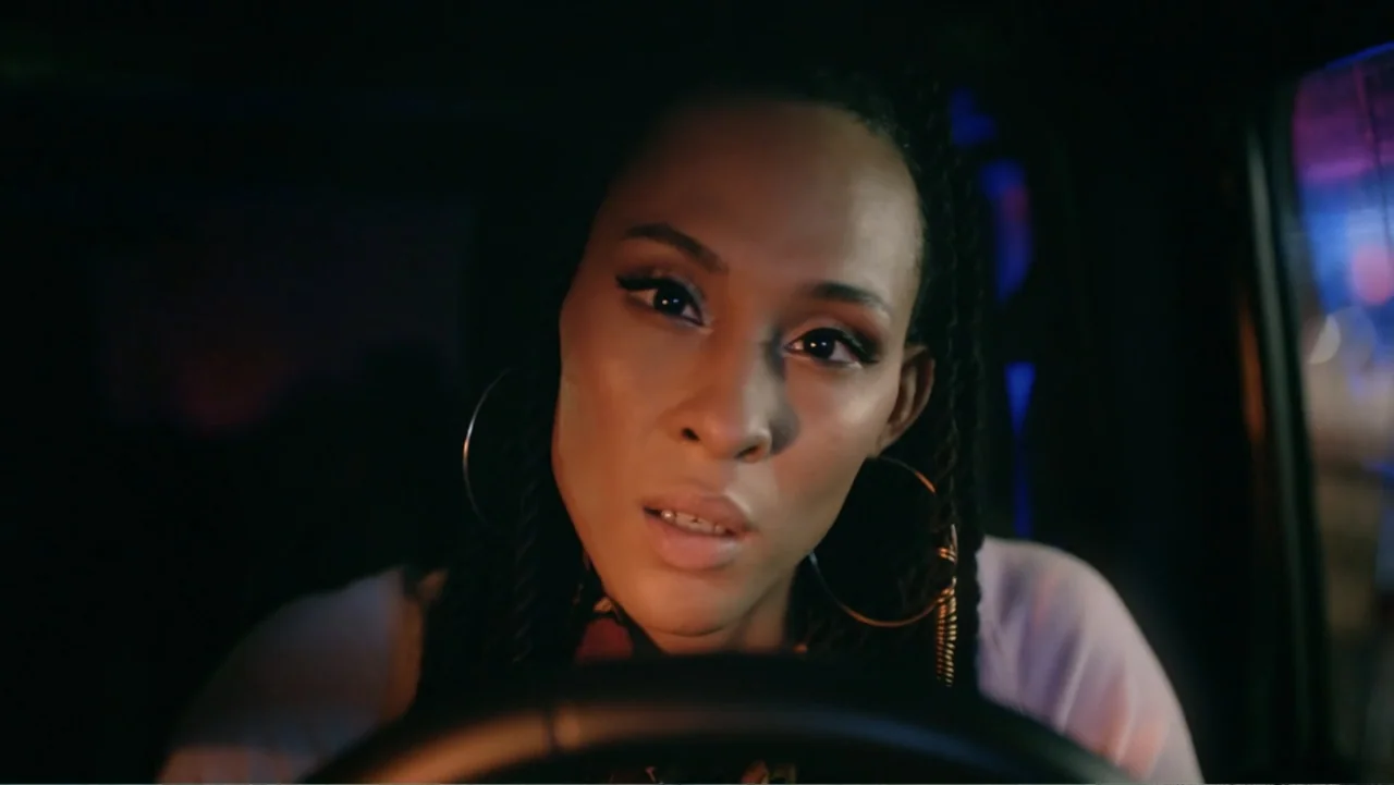 Between the World and Me (2020) movie still: closeup — A dark car interior at night with blurred colored light visible through the window. A woman…
