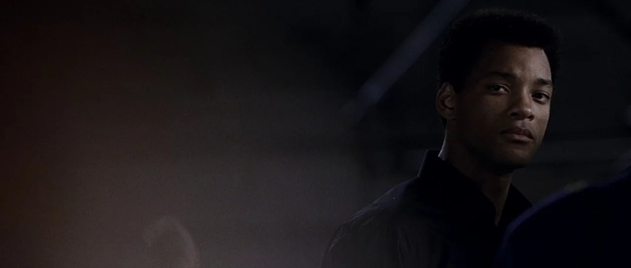 Ali (2001) movie still: medium — A man stands in a dimly lit, largely obscured space with dark surroundings. The subject is partially visible…