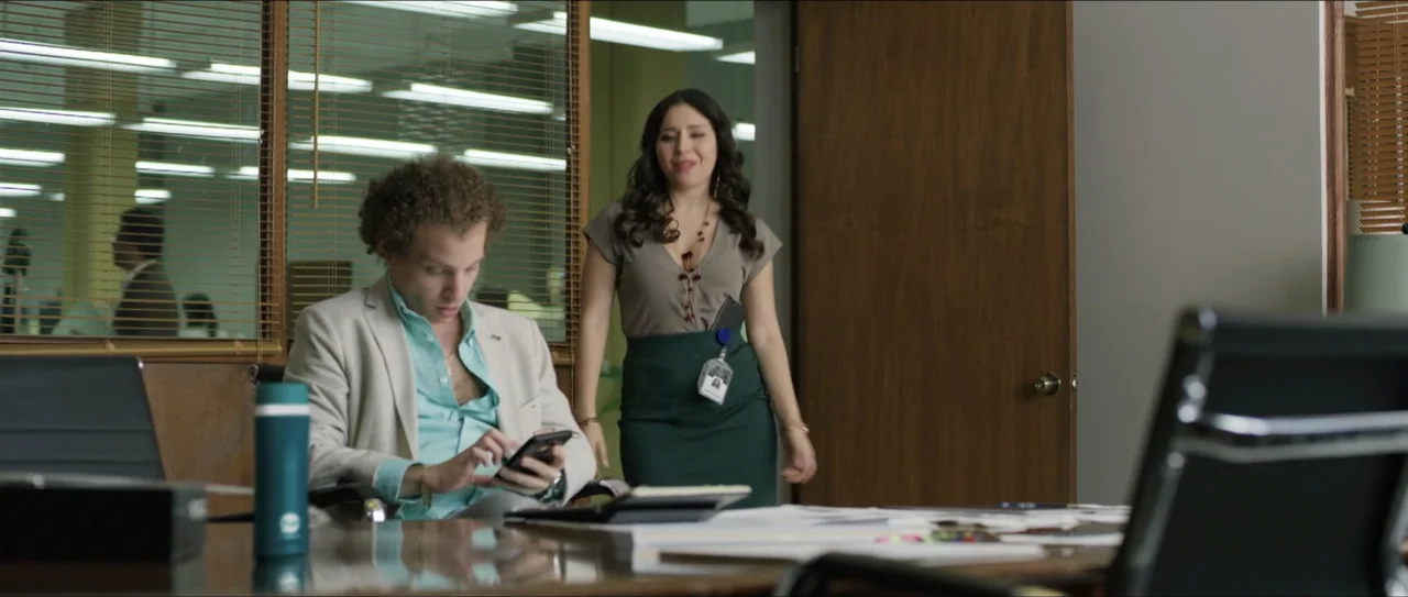 Mirreyes vs Godínez (2019) movie still: medium — An office interior features wood paneling, slatted window blinds, and scattered paperwork on a…