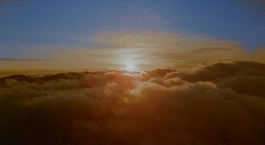Mishima: A Life in Four Chapters (1985) movie still: establishing — A dense layer of clouds sits below a bright sun setting on the horizon. The sky…