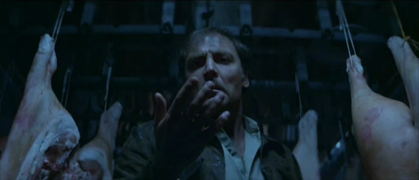 Roadgames (1981) movie still: medium — A dark industrial interior features numerous raw animal carcasses suspended from ceiling racks. A man stands…