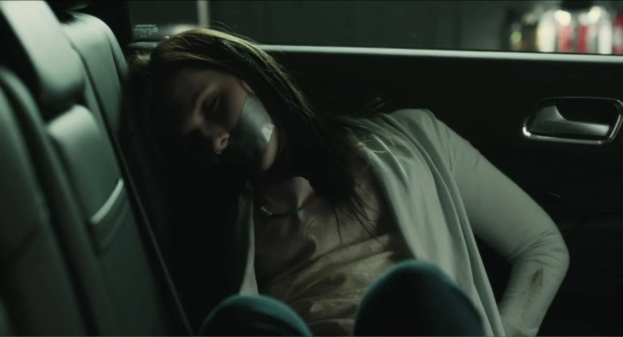 Haunter (2013) movie still: medium — A dark, modern car interior with black leather upholstery and a rear passenger seat. A young woman lies…