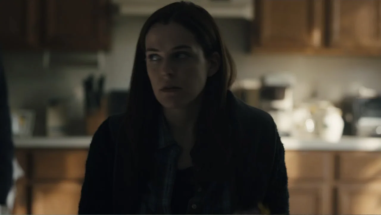 Paterno (2018) movie still: medium — A home kitchen featuring wooden cabinets and a blurred countertop in the background. A young woman stands…