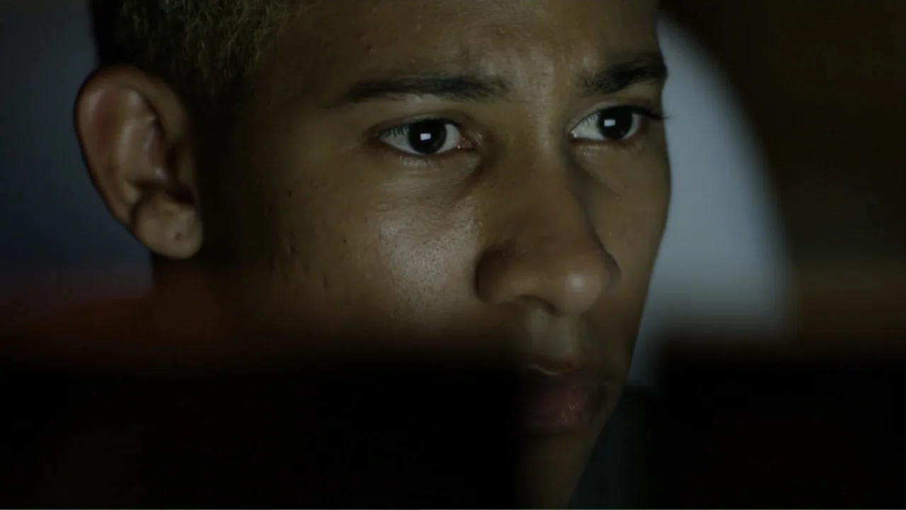 Like.Share.Follow. (2017) movie still: closeup — A dark indoor space where the only visible surface is a person's face. The subject looks at a…