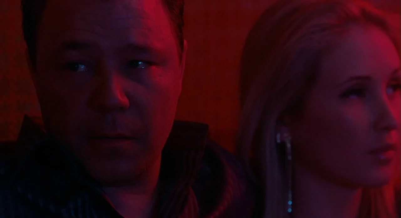 London Boulevard (2010) movie still: medium — A dimly lit, dark space glows with intense red light. A man and a woman sit together, both facing away…