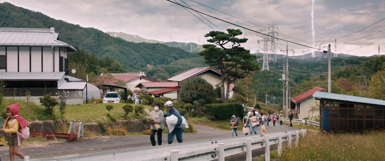 Shin Ultraman (2022) movie still: wide — A rural Japanese road runs through a mountainous valley with houses and power lines. A small group of…
