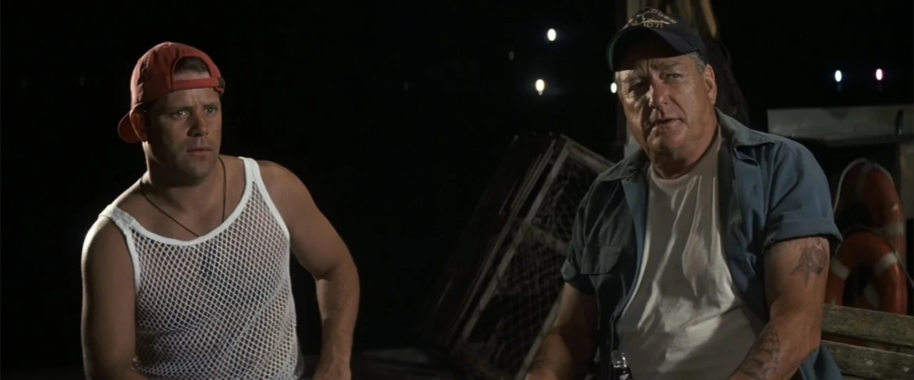 50 First Dates (2004) movie still: medium — A dark outdoor pier area at night with metallic wire lobster traps in background. Two men sit on a…