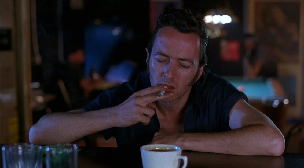 Mystery Train (1989) movie still: medium — A dark corner of a bar with pool tables visible in the blurred background. A man with eyes closed rests…