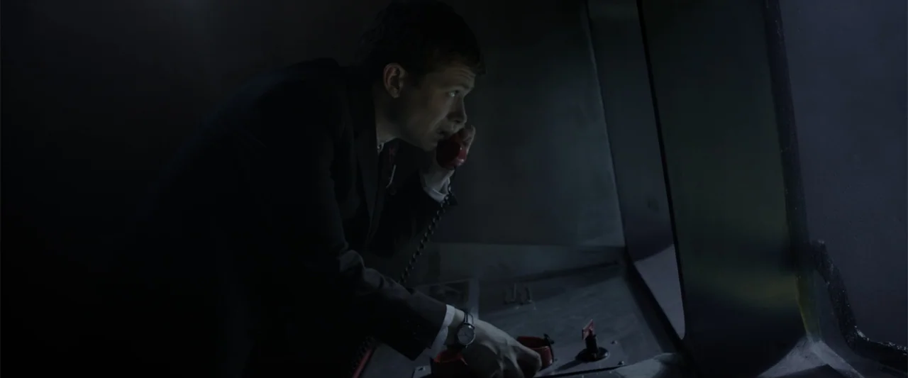 Howl (2015) movie still: medium — A dark console room with metallic surfaces and a large window facing outward. A man in a suit operates a red…
